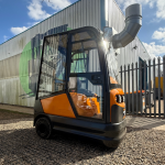 STILL R6-06 tow tractor in black and orange, featuring a fully enclosed cabin with glass doors. Ideal for indoor and outdoor towing in warehouses, factories, and logistics operations.