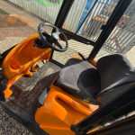 Interior of STILL R06-06 tow tractor in black and orange, featuring a fully enclosed cabin with glass doors. Parked outside an industrial warehouse under a blue sky. Ideal for indoor and outdoor towing applications in warehouses, factories, and logistics operations.