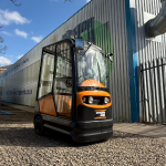 STILL R06-06 tow tractor in black and orange, featuring a fully enclosed cabin with glass doors. Ideal for indoor and outdoor towing applications in warehouses, factories, and logistics operations.